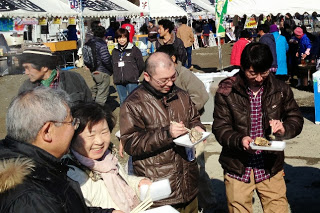 来場者たちが皿に盛られた牡蠣を手に取り、楽しそうに食べている様子の写真