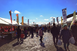 両側に並ぶ多くの屋台の間を来場者が歩いており、カラフルなのぼり旗が立ち並ぶ晴天の会場の様子の写真