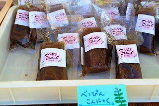 トレーに手書きの水色のポップが書かれ、白いトレーの中に「べっぴんこんにゃく」と書かれたラベル付きの茶色い長方形の個包装商品が並んでいる写真