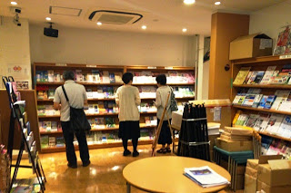 奥と右側の壁に設置された棚の前に立つ三人の来館者が、観光パンフレットを手に取って見ている様子の写真