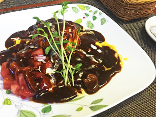 葉っぱの絵が載った白い角皿に盛り付けられた、オムライスにトマトとデミグラスソースがかかった料理の写真