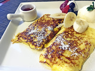 白い角皿に盛り付けられた2つのフレンチトーストに、アイスクリームやホイップクリーム、果物とシロップが入った容器が添えられている写真