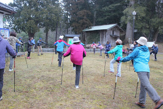 広場でノルディックウォーキングポールを使った準備体操が行われている様子の写真