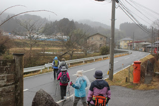 ポストと石碑がある交差点から、2車線の道路に、1列になって歩き出した参加者たちの写真