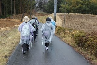 畑の間の道を2列になって歩いている参加者たちの後ろ姿の写真