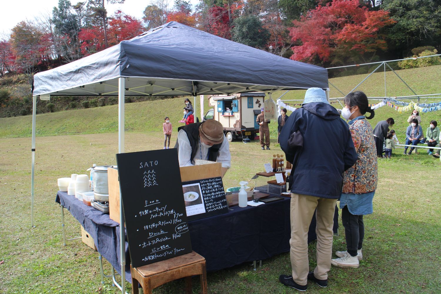 テントの下で店主が準備をしており、来場者が商品を選んでいる様子が写っている写真
