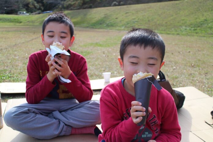 赤いトレーナーを着ている2人の男児が、笑顔でクレープをおおばっている様子の写真