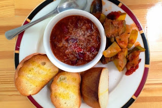 白いスープ皿に入ったトマト系の煮込み料理と、付け合わせのラタトゥイユやオイルがかけられたバゲットが並ぶ、洋風ランチプレートの写真