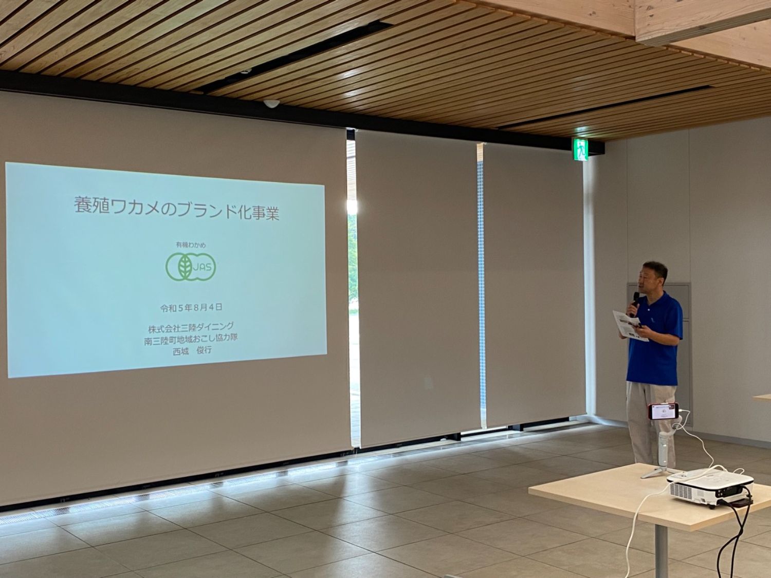 男性が室内で「養殖ワカメのブランド化事業」と題したスライドを示しながら説明している写真