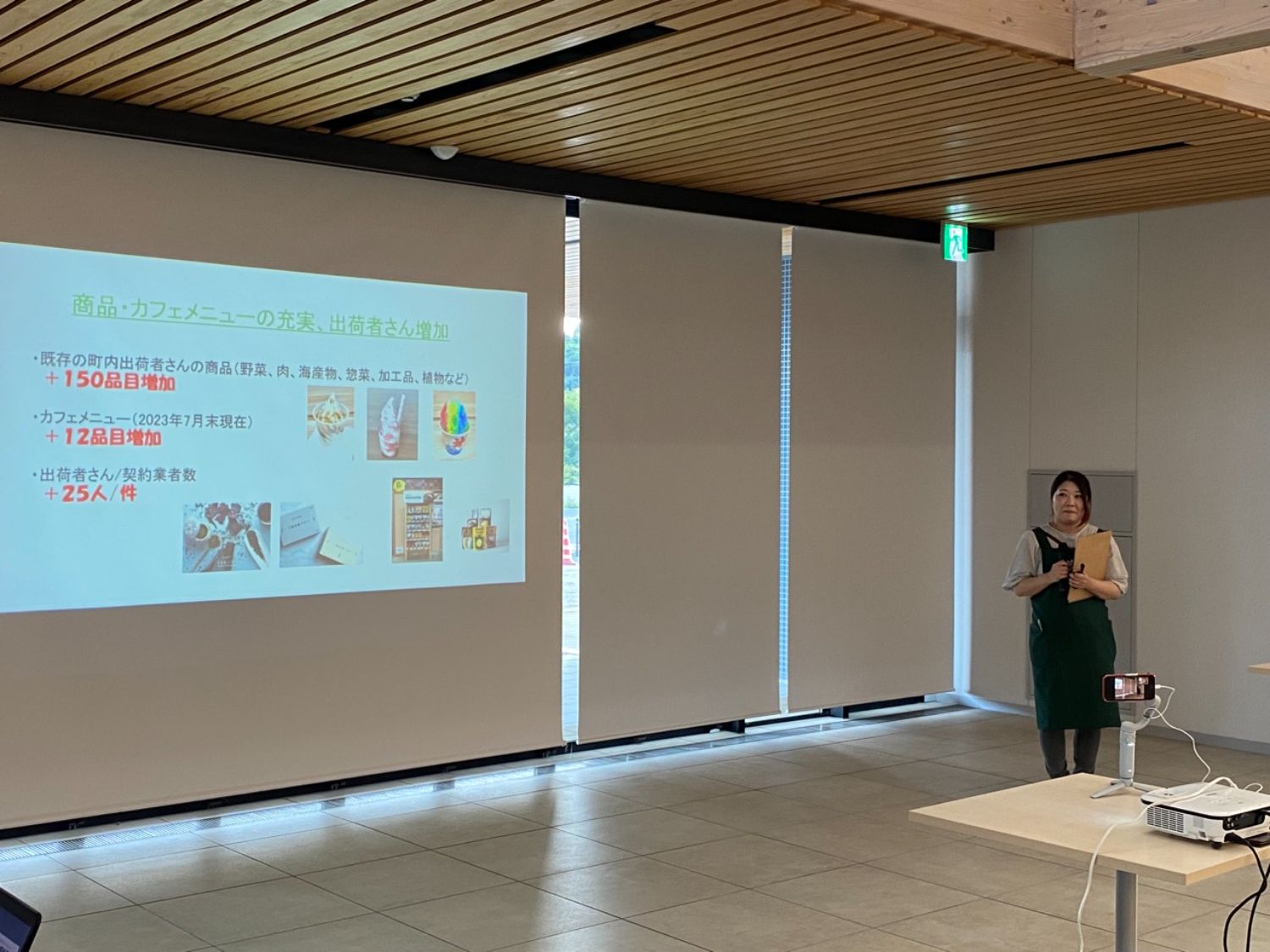 裕さんがエプロンを着て、資料を持ちながらスライドの前で話している写真