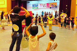 子どもたちと大人がステージに向かって手を挙げて踊っている様子の後ろ姿の写真