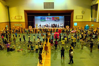 体育館内で多くの人々が輪になり盆踊りを踊っている、体育館全体を上から見下ろすように撮られた様子の写真