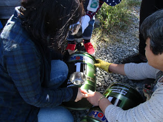 2人の参加者が協力して、ペール缶の側面に煙突部品を差し込んでロケットストーブを組み立てている写真