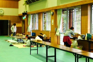 屋内施設で、人々が窓際に荷物を広げたり、作業をしたりしている様子の写真