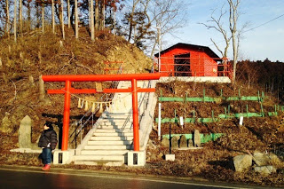 赤い鳥居が階段の下に立ち階段は丘の上にある小さな赤い建物へと続き階段の両側には手すりが設置されている写真