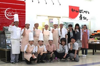 ショーケースの前に制服姿のシェフや店員が2列に並び、笑顔でガッツポーズをしている写真