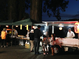 屋台の灯りに照らされて「やきとり」と書かれた提灯のある移動販売車の前で、子ども連れの客が注文している写真