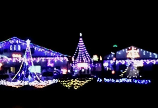 夜の暗闇の中で、建物の屋根や窓の輪郭に沿って青や紫、黄、白などのカラフルなクリスマスライトが輝き、中央にはツリー型のライト装飾が立ち、全体が華やかで明るい雰囲気に包まれたイルミネーションの様子の写真