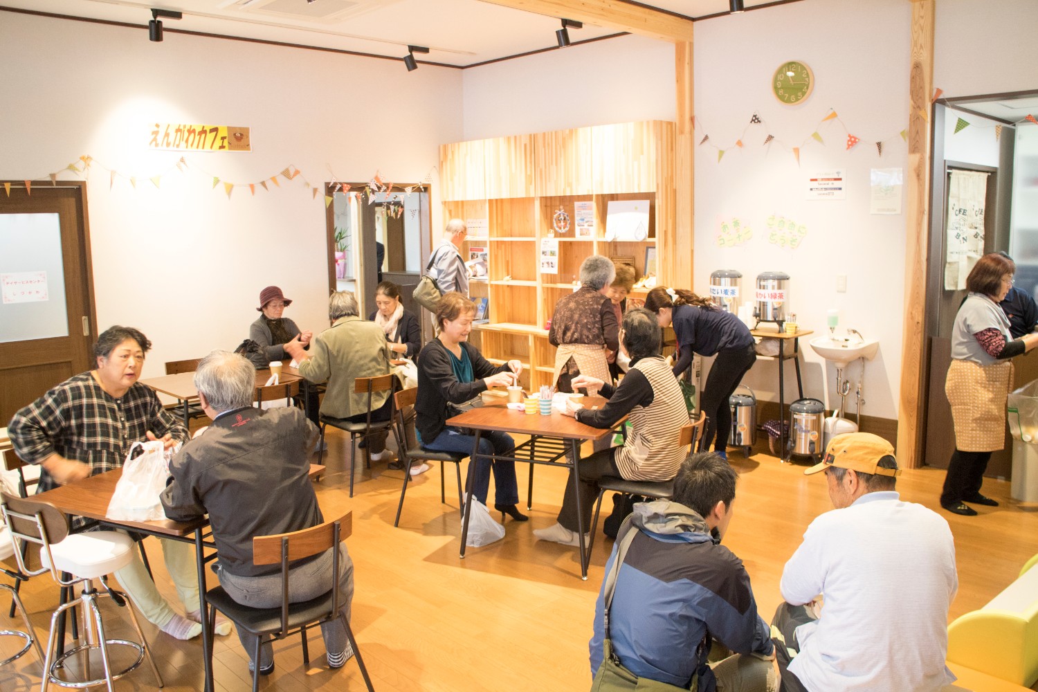 白い壁に「えんがわカフェ」と書かれた室内、来場者がテーブルを囲んで飲食や会話を楽しんでいる様子の写真