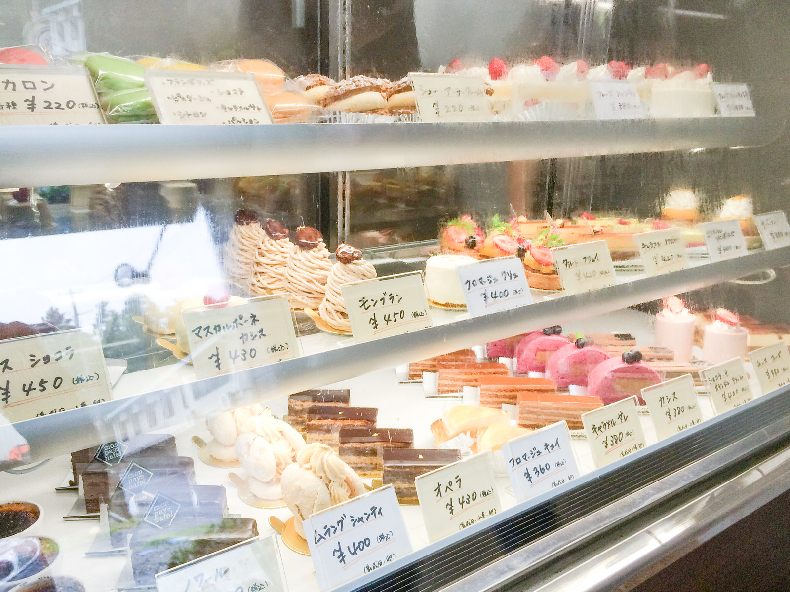 3段のショーケースに色とりどりのマカロン、シュークリーム、様々な種類のケーキがずらっと並んでいる写真