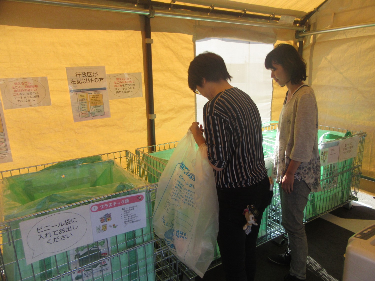 テントの中にゴミ箱と説明書きがあり、女性2人がゴミを分別している様子の写真