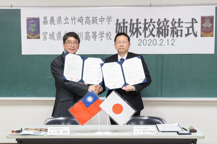 日本と台湾の高校の代表者が、姉妹校提携の調印式で契約書を手に持ち、握手している写真