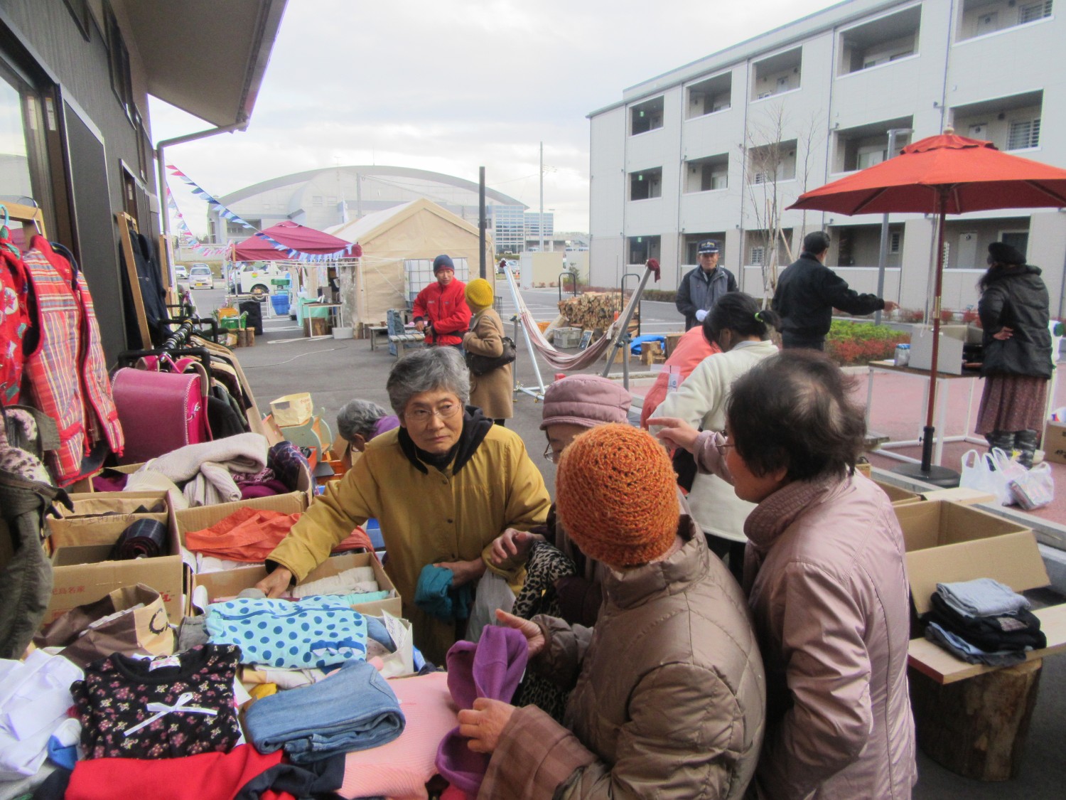 段ボールの箱の中に衣類や使わない食器が積み込まれ、服を選んでいる人々の写真