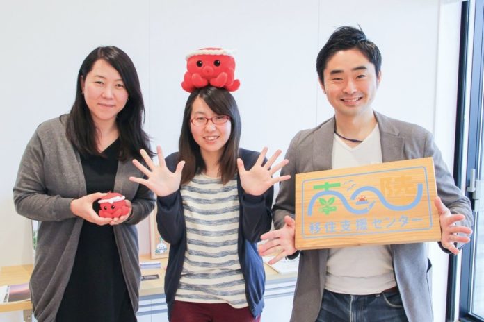 赤いぬいぐるみを頭に乗せたり、木の看板や赤いぬいぐるみを持っている3人の男女の写真