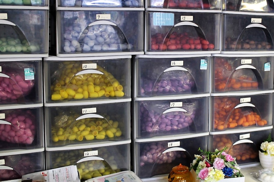 さまざまな色に染められたまゆ玉が透明なケース棚の中に納められている写真