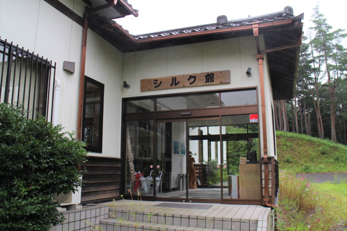 ガラスの自動ドアの上に「シルク館」という看板がかかった入口付近を写したシルク館の外観写真