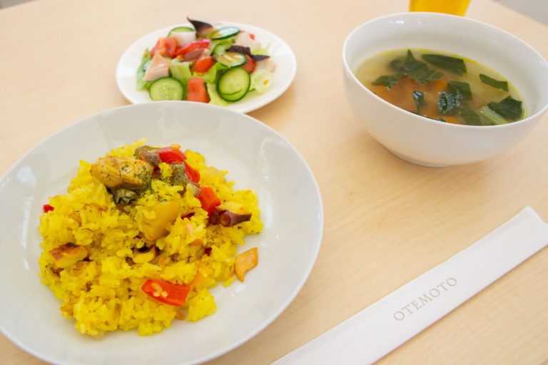 白い丸皿に牡蠣とタコと銀鮭のパエリア、タコと地元野菜のサラダ、スープ皿にホヤと小松菜のスープが盛り付けられた写真