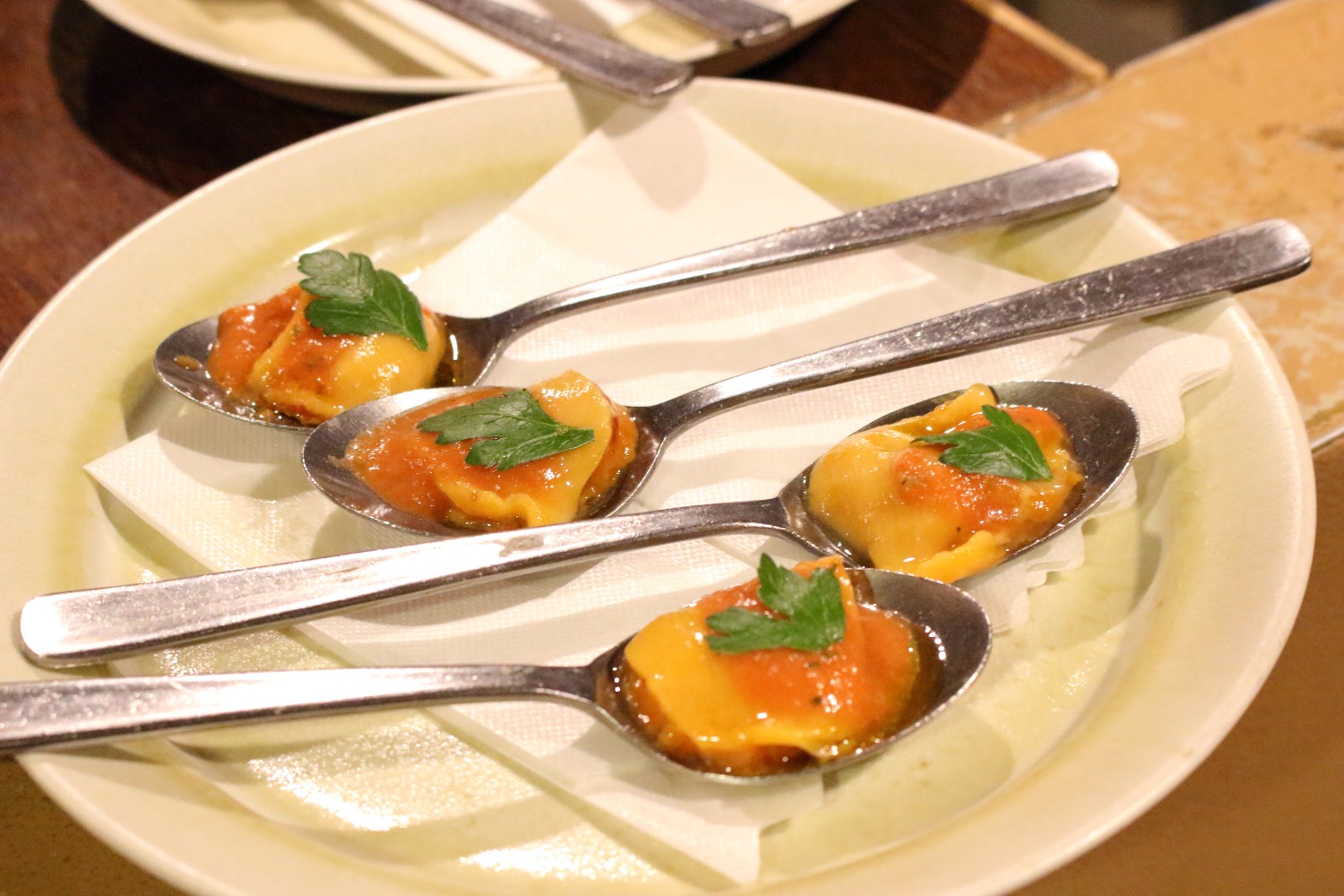 スプーンの上にパセリが添えられた一口サイズのホヤのカスパチョがトマトソースと共に盛られた前菜が四つ並んでいる写真