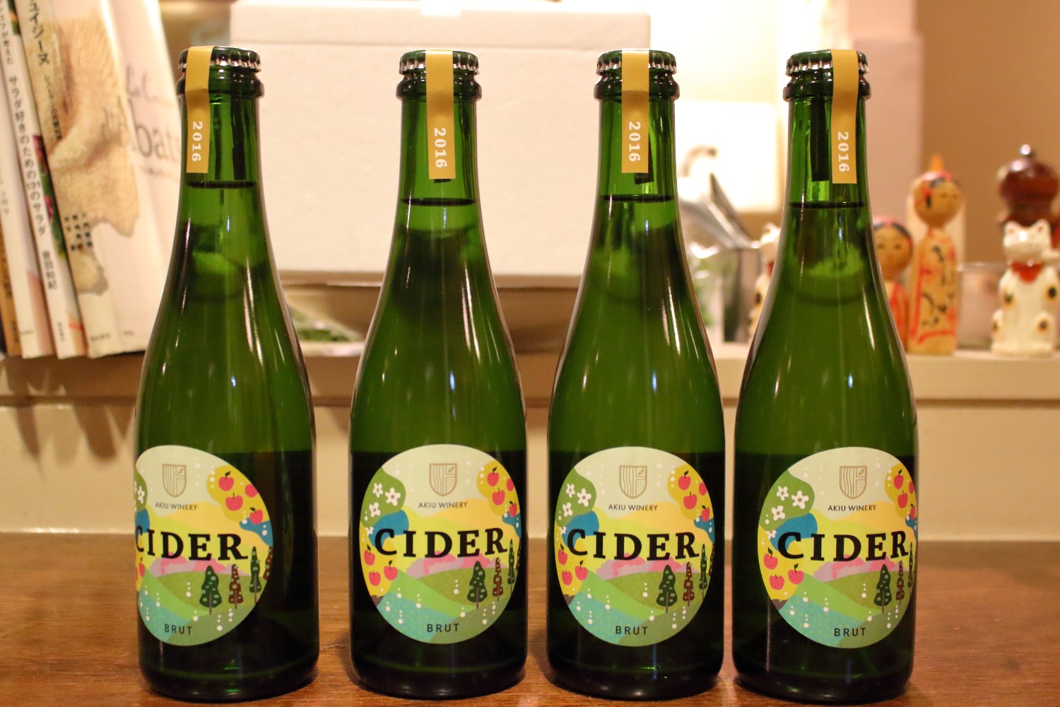 花やリンゴの実がなり、山や木々に囲まれた自然を描いたラベルの中央に「CIDER」と書かれた緑色の瓶が4本、カウンターの上にまっすぐ並べられている写真