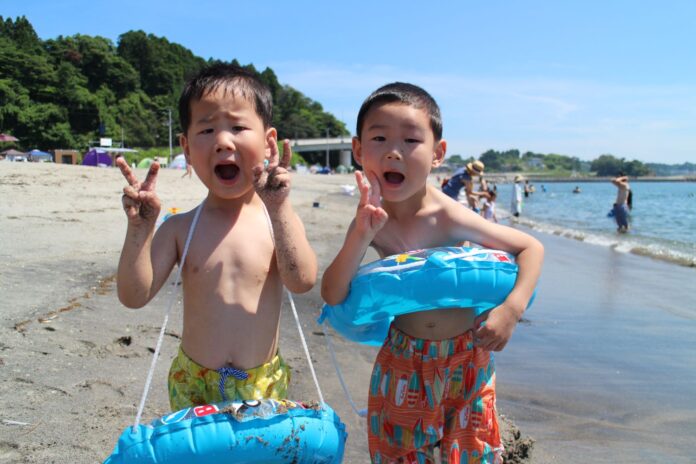 ビーチで浮き輪を持った男の子2人がカメラに向かってピースサインをしている写真