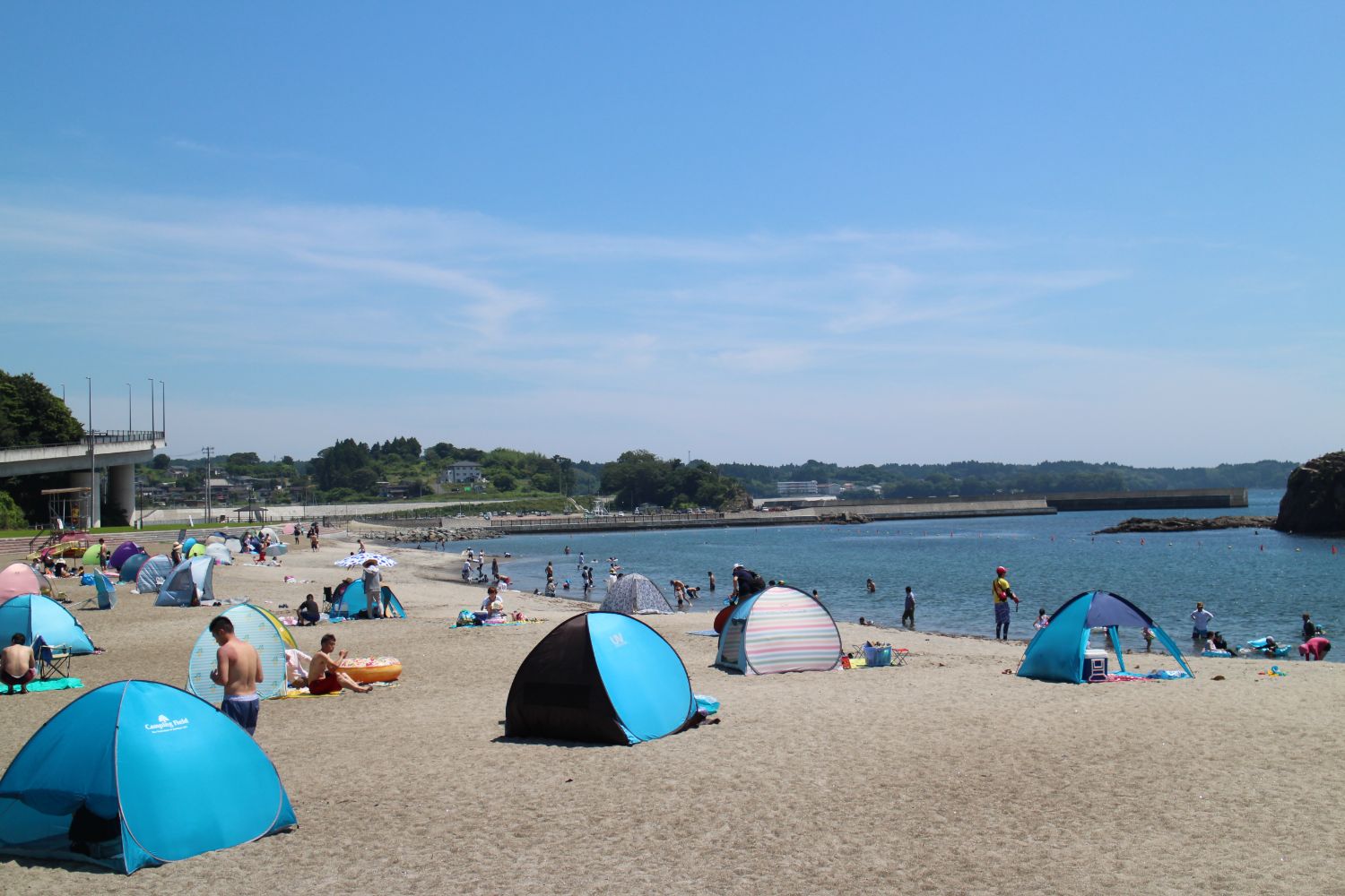 砂浜にたくさんのサンシェードテントが並び、多くの人たちで賑わっている海水浴場の写真