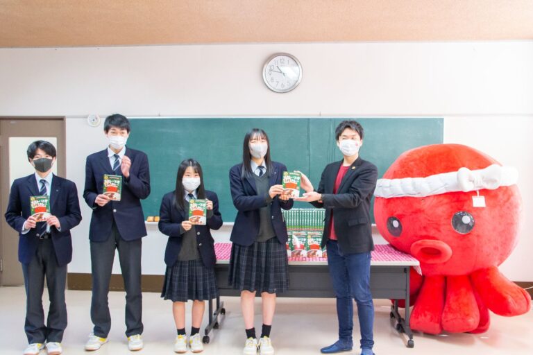 教室の黒板の前で、制服を着た4人の高校生と黒いジャケットを着た男性が一列に並び、全員が手に「オクトパス君合格カレー」のパッケージを持っていて、右端には白いハチマキを巻いた大きな赤いタコのキャラクター「オクトパス君」が立っている記念撮影の写真