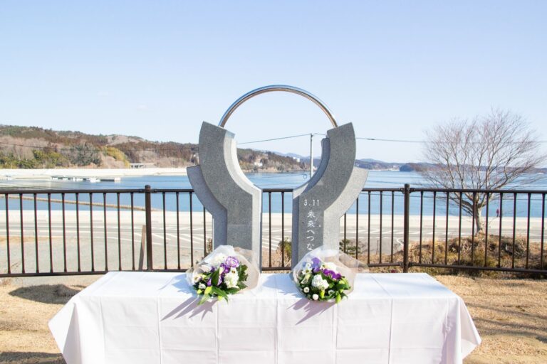 小高い丘や海が見渡せる献花台に2つの花束が置かれ、「3月11日未来へつなぐ」と刻まれた、両手で包み込んだような形の追悼モニュメントの写真