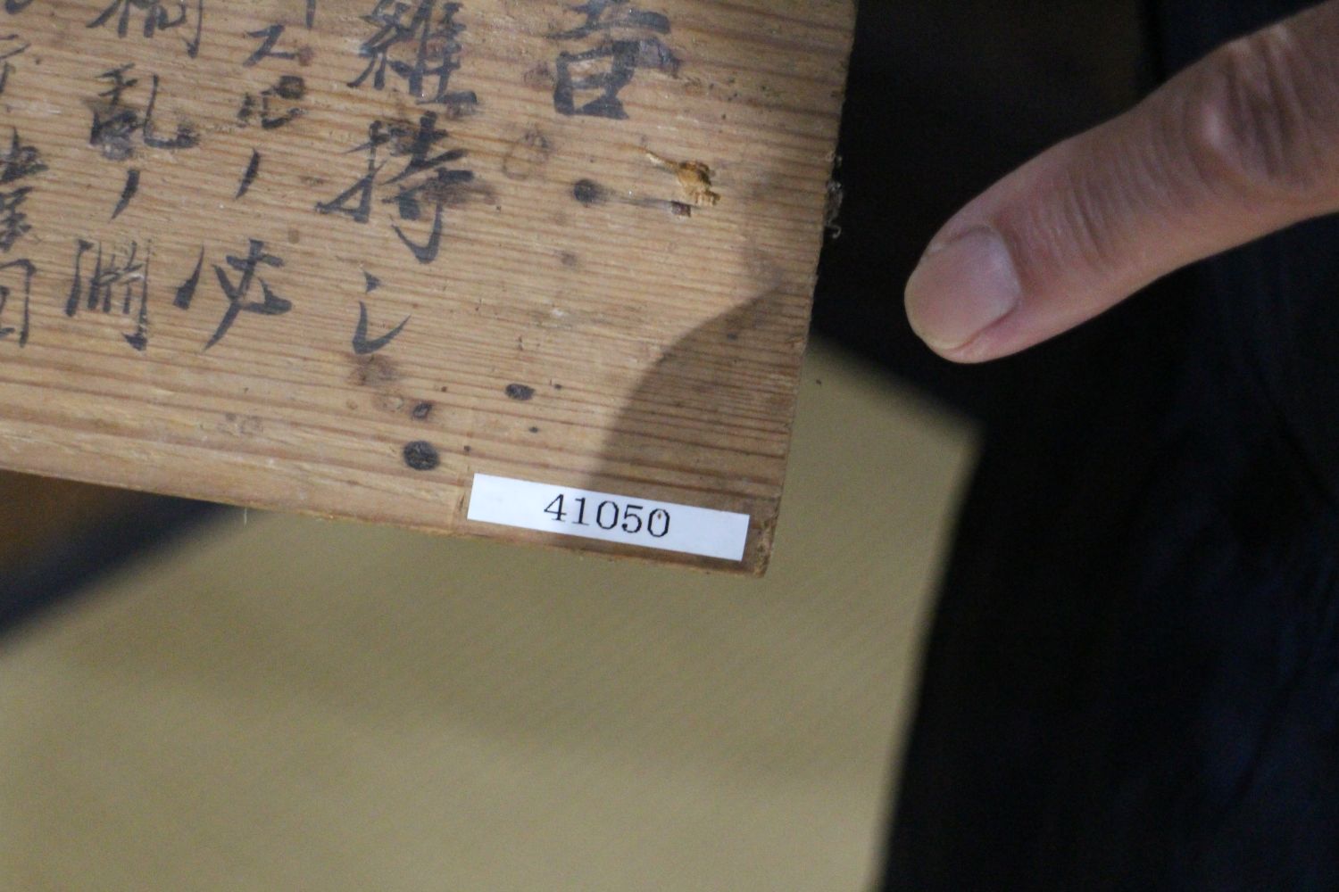 黒い墨で漢字が書かれている木の板の端に白いラベルで「41050」と数字が記され、指がそのラベルを指している写真