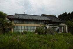 正面に長い窓が並び、黒い瓦屋根と薄い黄色の外壁を持つ大きな二階建て住宅の写真