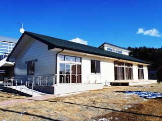 白い壁と黒い屋根の平屋建てで、家の前には手すり付きのスロープが設置されているコアラ館の外観写真