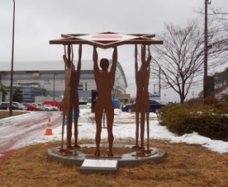 人型の彫刻が円形に配置され、それぞれが頭上で星の形を支えている復興祈願の彫像「栄光と再生の像」の写真