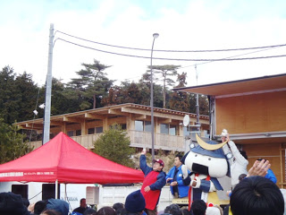 宮城観光PRキャラクターのむすび丸と関係者の方々がステージ上でイベントを行っている様子を写した写真