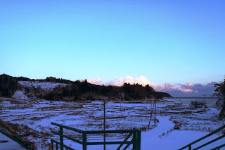 雪に覆われた沿岸部の広い平地を見渡す構図で、遠くに海と空が広がっている雪景色の風景を写した写真