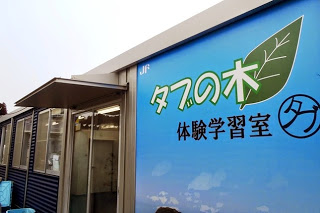 青い看板に「タブの木体験学習室」と書かれたプレハブ施設の入口を写した写真