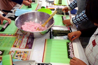 緑の巻きすの上で、ピンク色の酢飯を海苔の上に並べて巻き寿司を作っている写真