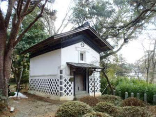 緑豊かな木々に囲まれた静かな庭園の中に建っている白壁に黒い格子があしらわれた伝統的な日本の蔵の写真