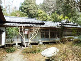 木々に囲まれた場所に建つ、瓦屋根で横長の趣のある日本家屋で、手前には庭が広がっている松笠屋敷の写真