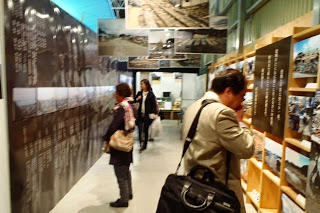 天井に大きな写真パネル、壁に沢山の写真が展示されている通路に立つ人たちが展示品を見ている写真