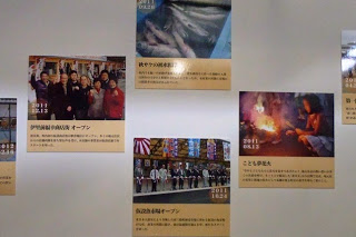 秋サケの水揚げや仮設魚市場オープンなど復興に進む様子の写真が大きく引き伸ばされたパネルが壁に展示されている写真