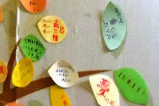 木の枝に貼り付けられたカラフルな色の葉っぱの形をした色紙に沢山のメッセージが書かれている様子をアップで撮影した写真